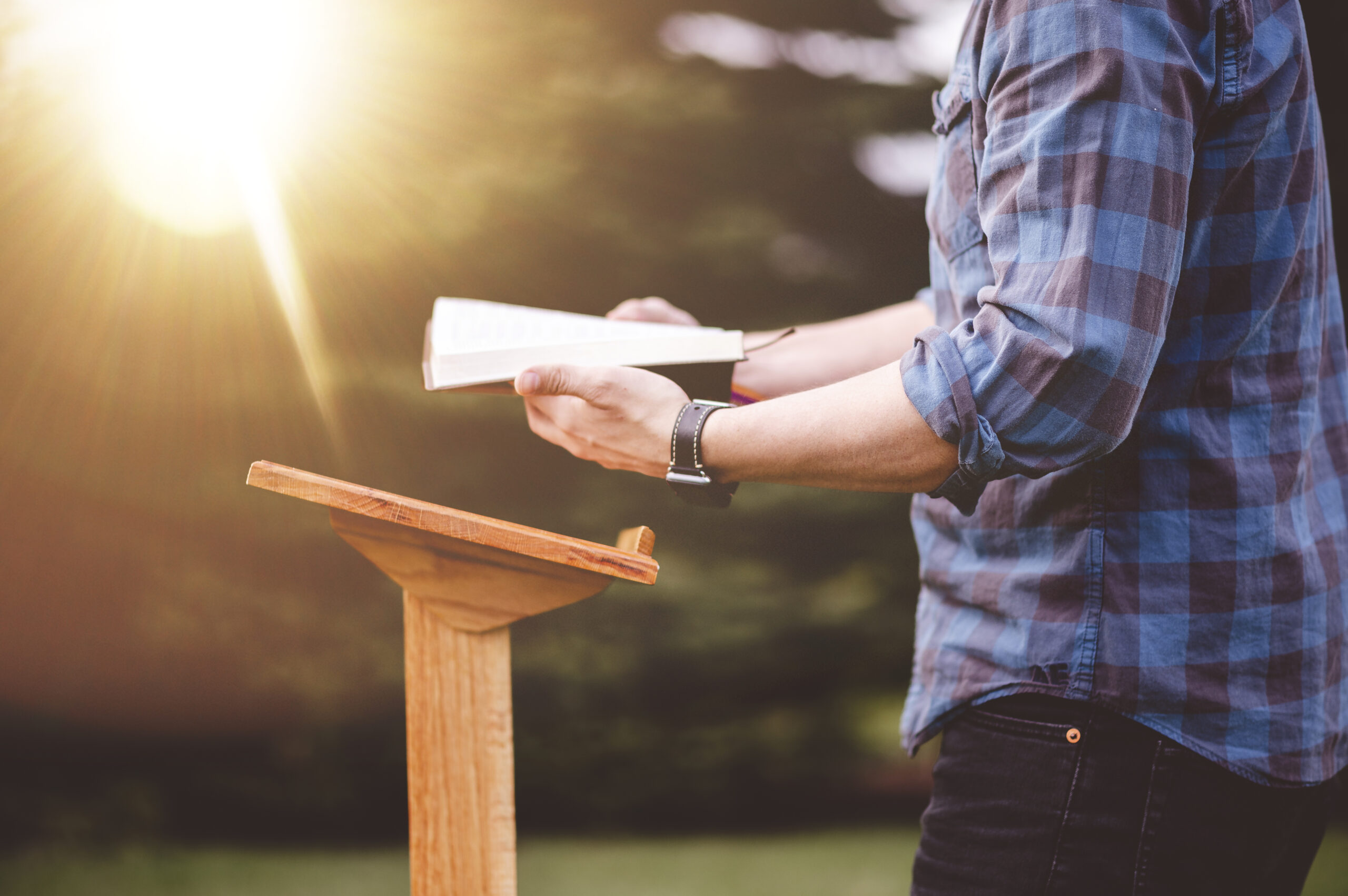 a-shallow-focus-shot-of-a-male-reading-the-bible-while-standing-near-a-podium